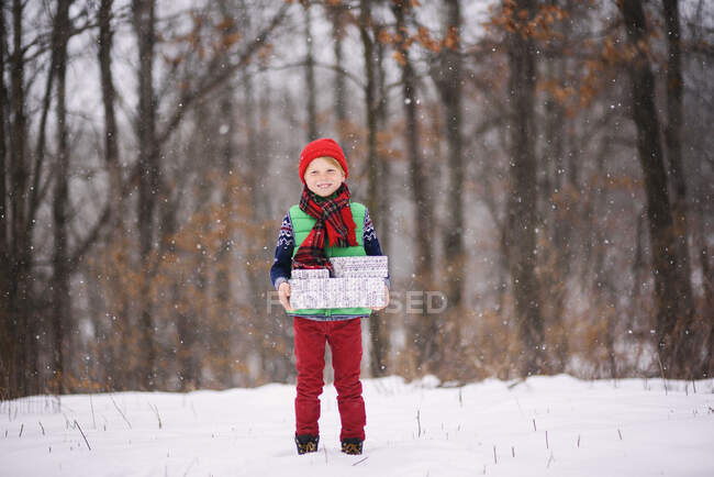 Boy standing in snow carrying Christmas gifts — Stock Photo