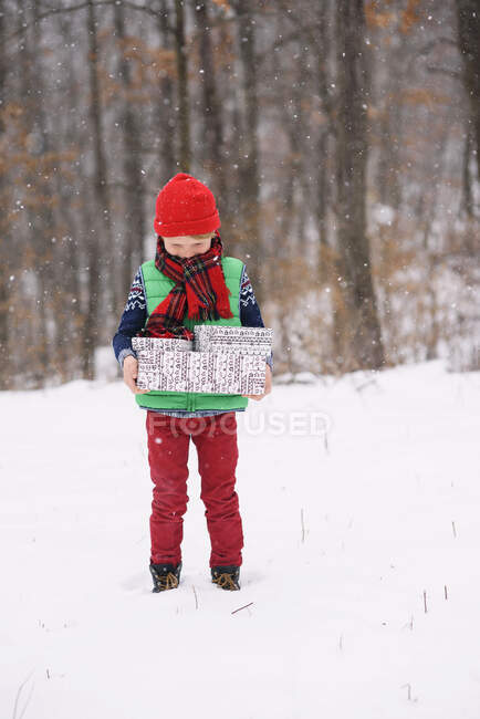 Boy standing in snow carrying Christmas gifts on winter day — Stock Photo