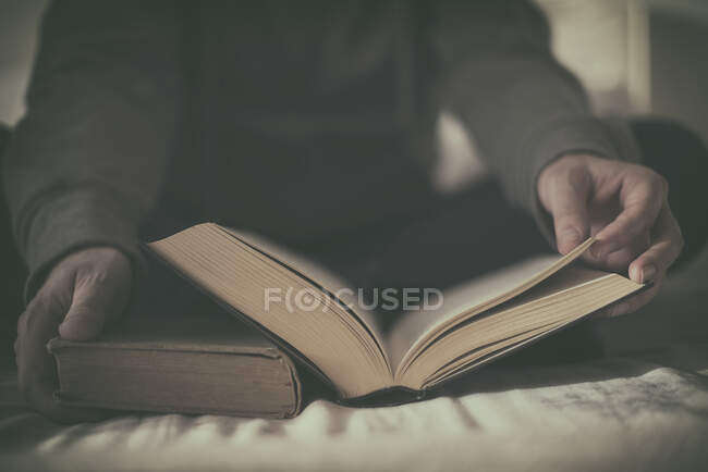 Человек, сидящий на кровати и читающий книгу — стоковое фото