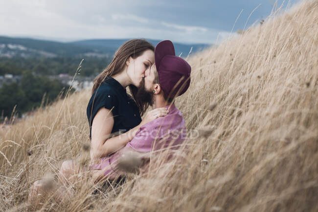 Couple sitting in a field kissing — Stock Photo