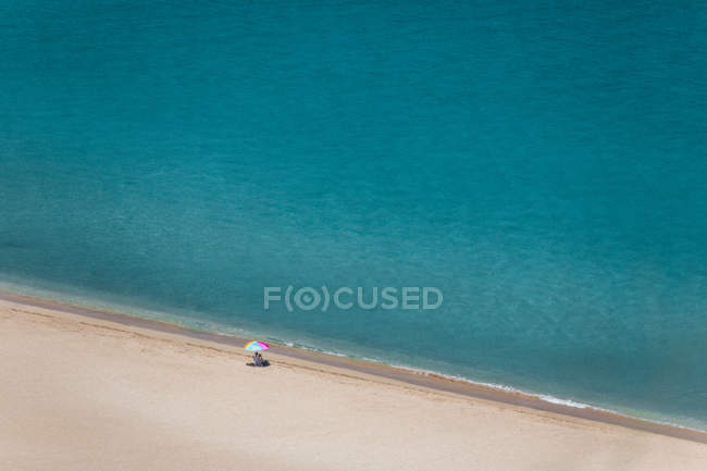 Mujer mayor sentada en la playa bajo una sombrilla, Waimea Bay, Oahu, Hawaii, America, USA - foto de stock