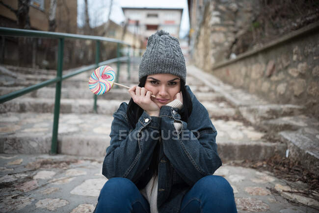 Portrait of a woman sitting on steps holding a lollipop — Stock Photo