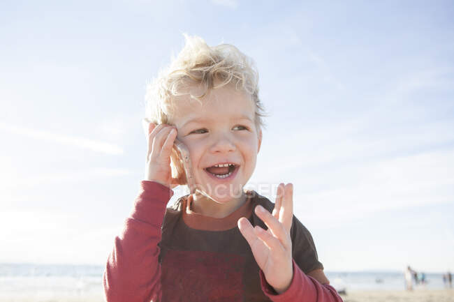 Ragazzo sorridente in piedi sulla spiaggia che parla su un telefono cellulare, Orange County, California, Stati Uniti — Foto stock