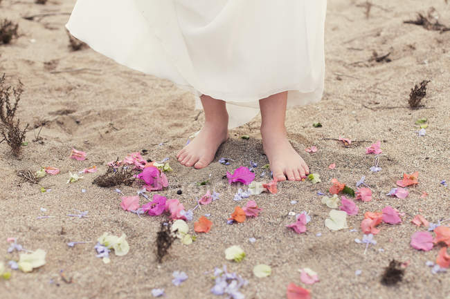 Ragazza a piedi nudi nella sabbia circondata da petali di fiori — Foto stock