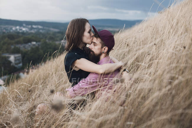 Mulher sentada em um campo beijando seu namorado — Fotografia de Stock
