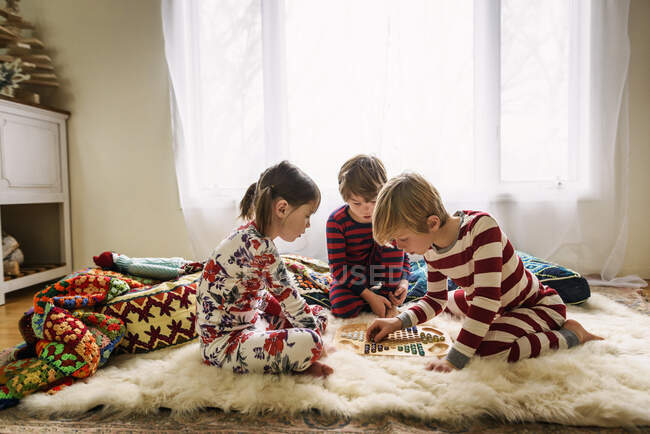 Трое детей сидят на полу и играют в настольную игру. — стоковое фото
