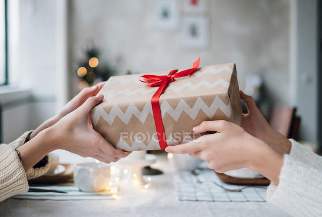 Abgeschnittenes Bild von Frauen, die ihrem Freund ein verpacktes Weihnachtsgeschenk machen — Stockfoto