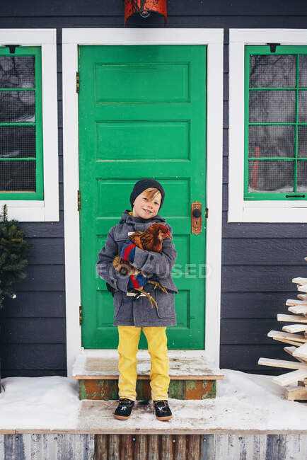 Хлопчик стоїть біля будинку, що тримає курку — стокове фото