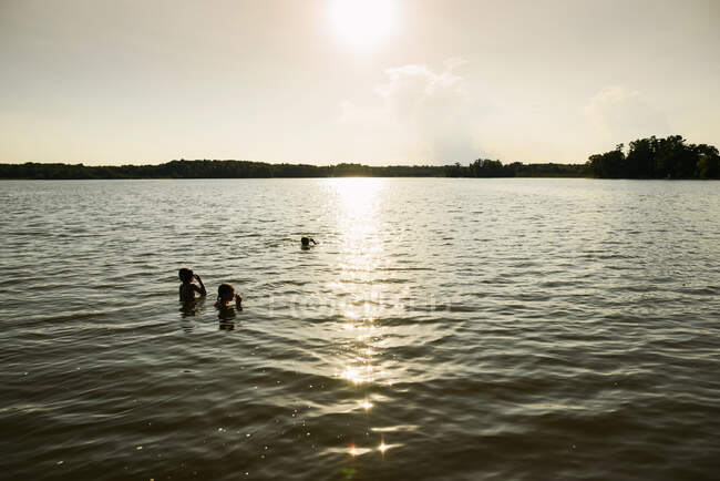 Three children swimming in a lake at sunset — Stock Photo