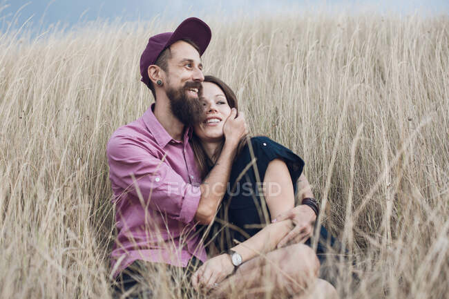 Paar sitzt auf einem Feld und umarmt sich — Stockfoto