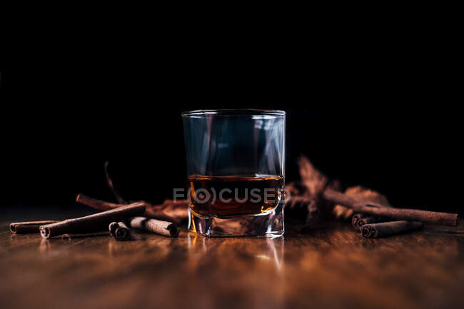 Whiskey con canela y hielo sobre fondo negro - foto de stock