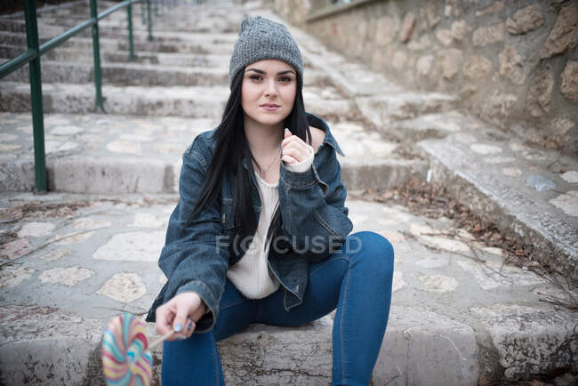 Portrait of a woman sitting on steps holding a lollipop — Stock Photo