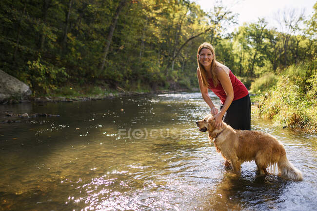 Donna in piedi in un fiume con un cane golden retriever — Foto stock
