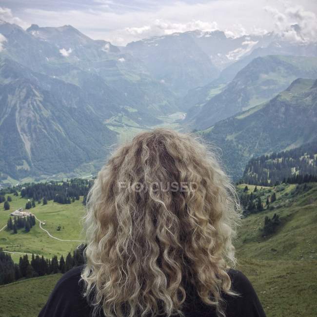 Вид сзади на женщину с вьющимися волосами, смотрящую на горы — стоковое фото