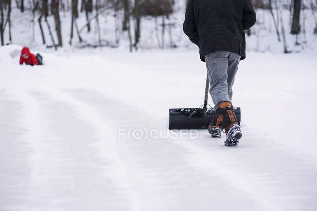 Hombre paleando nieve mientras su hijo construye un fuerte de nieve - foto de stock