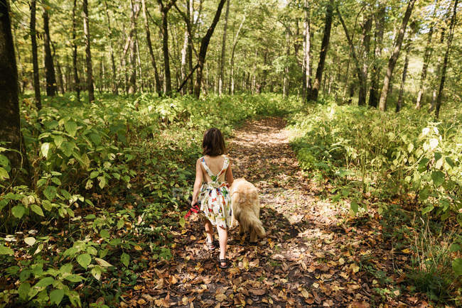 Fille marche à travers la forêt avec son chien golden retriever — Photo de stock