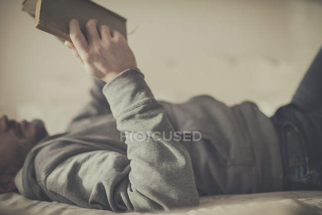 Man lying on a bed reading a book — Stock Photo