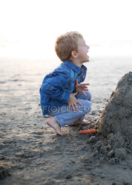 Happy boy building a sandcastle on the beach, Orange County, California, Estados Unidos - foto de stock