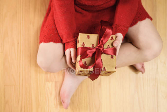 Ansicht eines Mädchens im Schneidersitz, das ein verpacktes Weihnachtsgeschenk in der Hand hält — Stockfoto