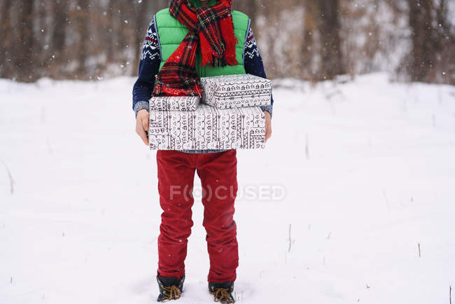 Immagine ritagliata del ragazzo in piedi nella neve portando regali di Natale — Foto stock