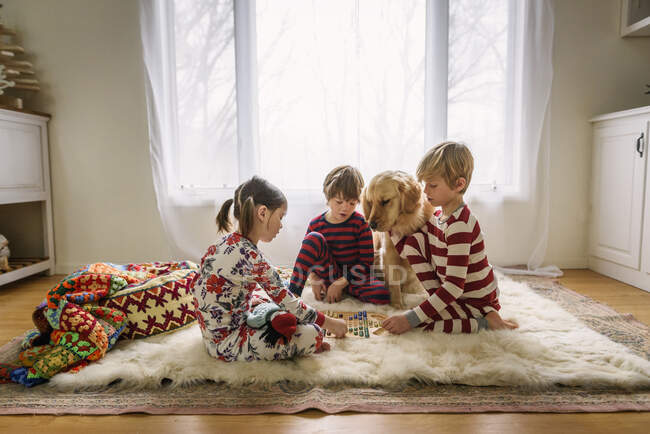 Três crianças sentadas no chão com seu cão golden retriever jogando um jogo de tabuleiro — Fotografia de Stock