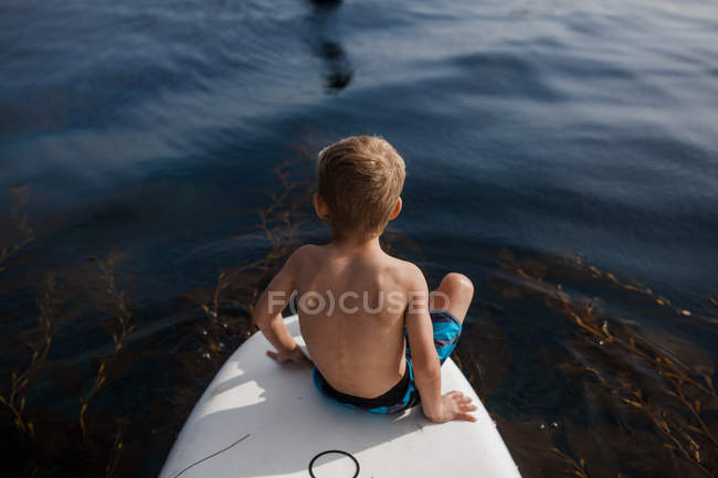 Niño sentado en un paddleboard, Condado de Orange, California, Estados Unidos - foto de stock
