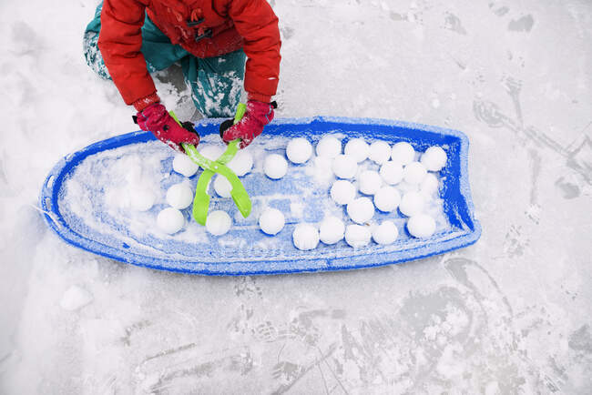 Fille assise à côté d'un traîneau faisant des boules de neige — Photo de stock