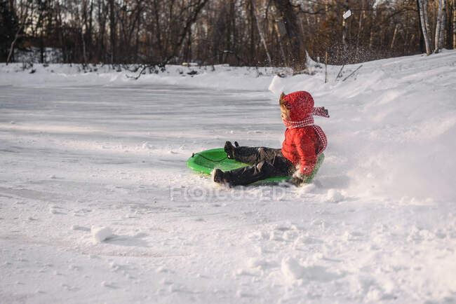 Мальчик катается на санках по снегу в зимний день — стоковое фото