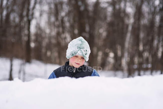 Niño de pie en el bosque construyendo un fuerte de nieve - foto de stock