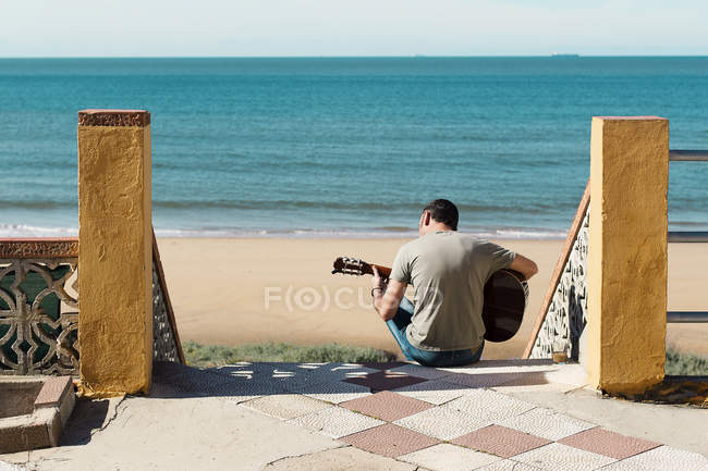 Чоловік сидить на сходах біля пляжу і грає на гітарі (Іспанія). — стокове фото