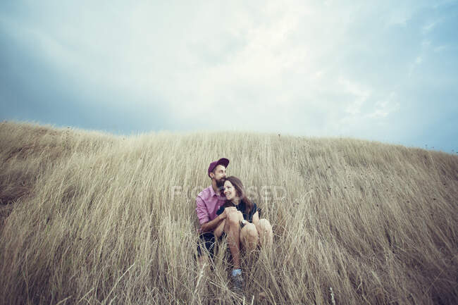 Casal sentado em um campo abraçando — Fotografia de Stock
