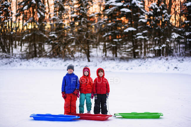 Троє дітей стоять у снігу зі своїми санчатами — стокове фото