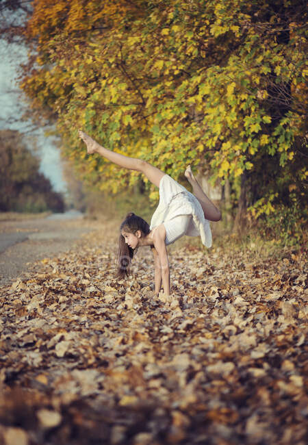 Girl standing upside down in autumn leaves doing yoga — Stock Photo