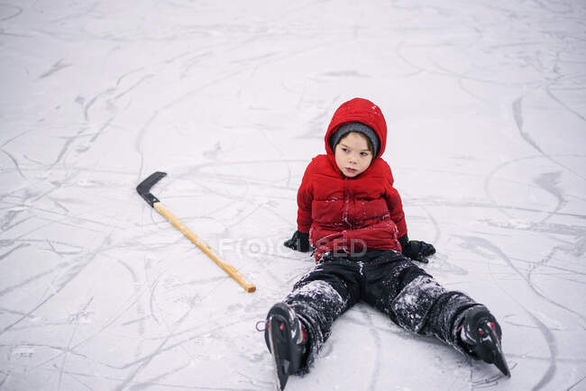 Мальчик сидит на льду с хоккейной клюшкой — стоковое фото