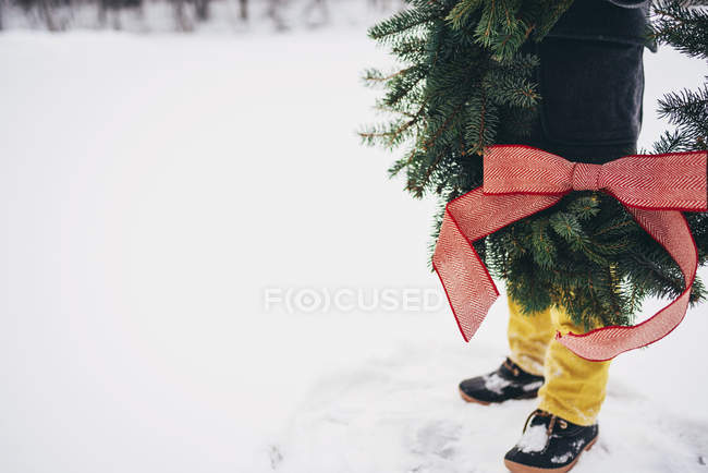 Обрізаний образ хлопчика стоїть в снігу тримає Різдвяний вінок — стокове фото