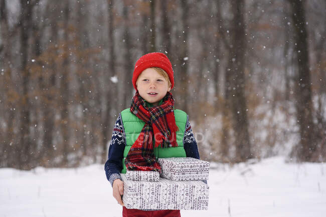 Junge steht im Schnee und trägt Weihnachtsgeschenke — Stockfoto