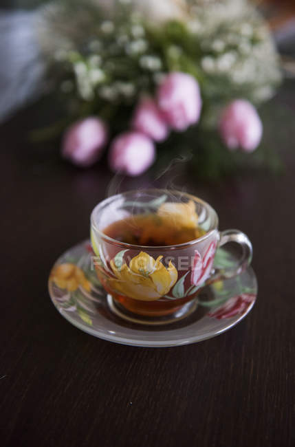 Vista de cerca de la taza de té caliente y tulipanes - foto de stock