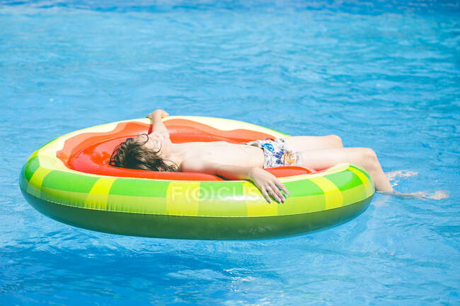 Junge liegt auf einer aufblasbaren Luftmatratze aus Wassermelone in einem Schwimmbad — Stockfoto