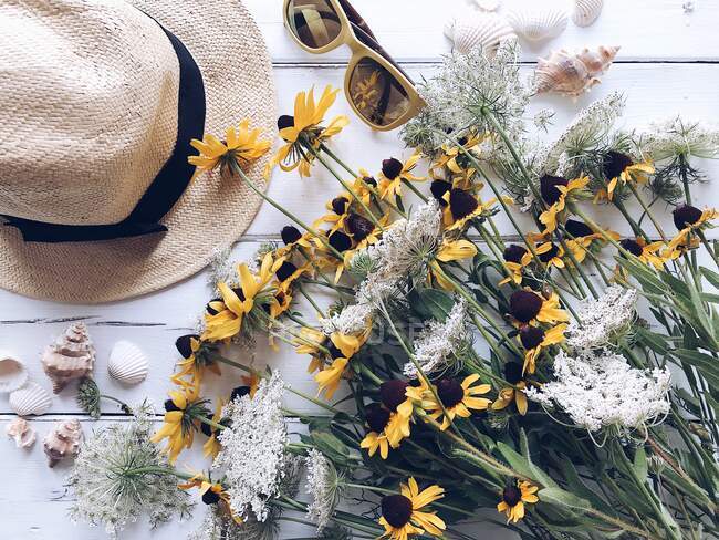 Flores silvestres, sombrero de paja, gafas de sol y conchas marinas - foto de stock