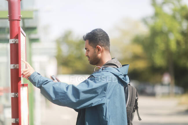 Homem de pé em uma parada de ônibus olhando para o calendário, Alemanha — Fotografia de Stock