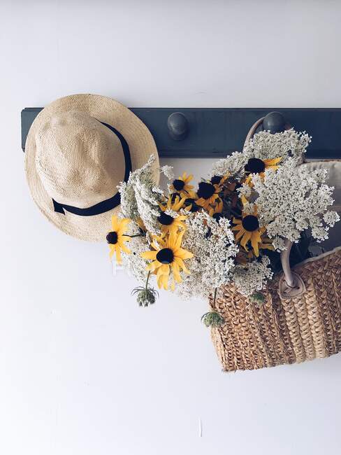 Ramo de flores en una cesta colgada en un perchero con un sombrero - foto de stock