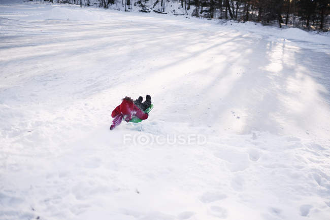 Мальчик катается на санках по снегу зимой — стоковое фото