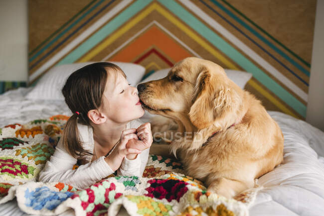Young girl playing with dog on a bed — Stock Photo