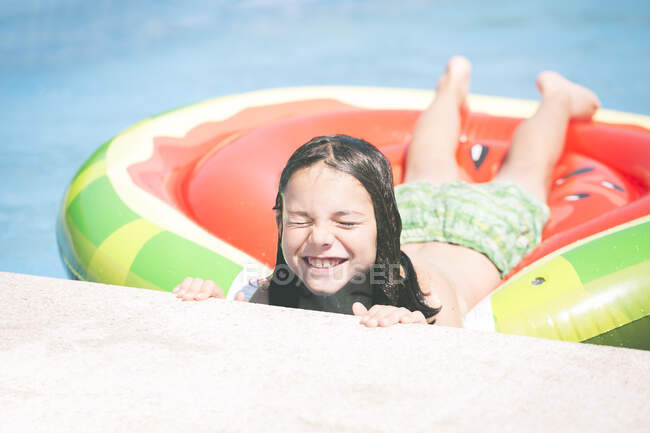 Улыбающийся мальчик на надувном арбузе в бассейне — стоковое фото