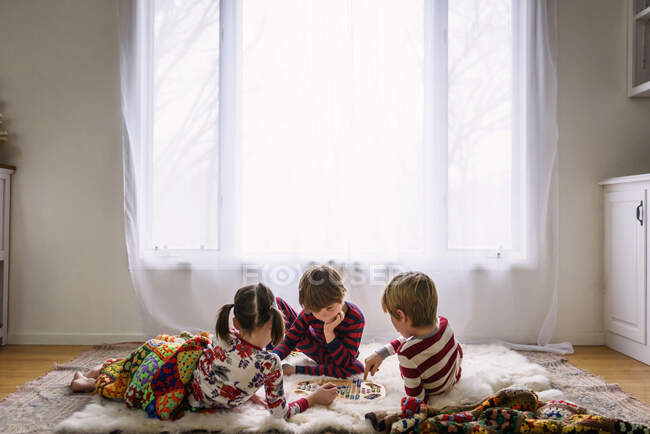 Tres niños tumbados en el suelo jugando un juego de mesa - foto de stock