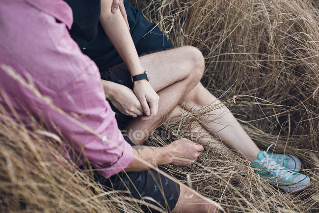 Couple assis dans un champ et tenant la main — Photo de stock