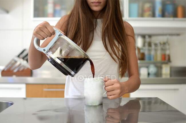 Chica vertiendo una taza de café en la cocina - foto de stock