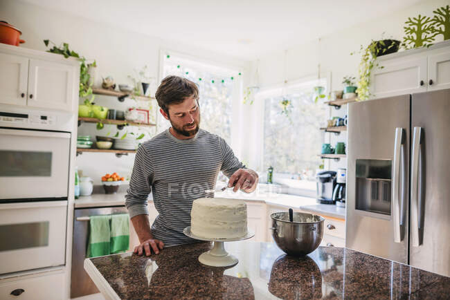 Homem de pé na cozinha decorando um bolo — Fotografia de Stock