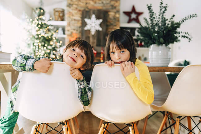 Niño y niña sentados en la mesa de comedor jugando en Navidad - foto de stock