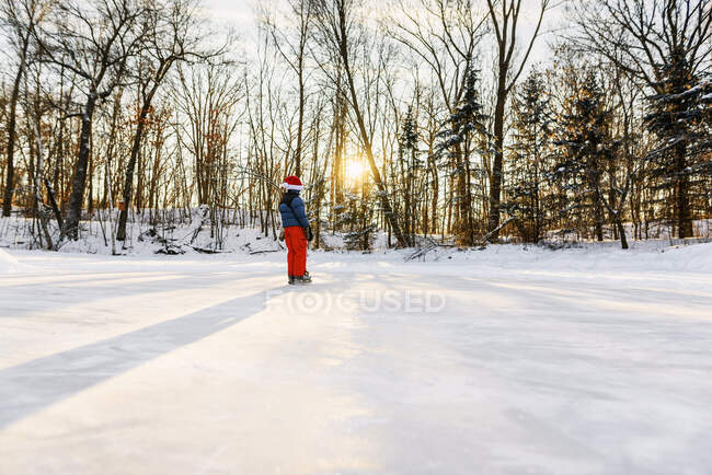 Мальчик в шляпе Санты катается на коньках по замерзшему озеру — стоковое фото